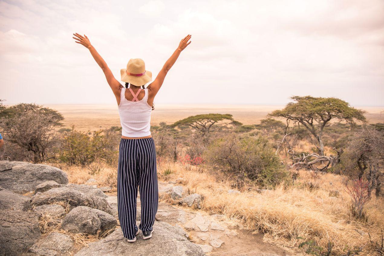 Eine Frau mit ausgebreiteten Armen blickt über die weiten Ebenen der Serengeti, ein unvergesslicher Moment auf einer Tansania Safari.